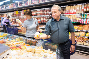 Elderly man choose cheese in supermarket
