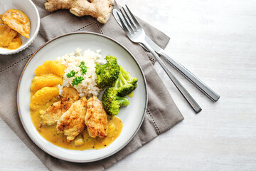 Fried chicken fillet in orange ginger sauce with broccoli vegetables and rice, on a plate with...