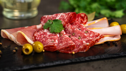 Fresh slices cold cuts, sausage ham bacon jamon on stone cutting board with olives and parsley. Meat pork beef. Food