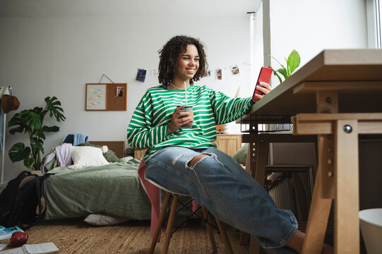 Happy teenage girl using smart phone at desk in bedroom