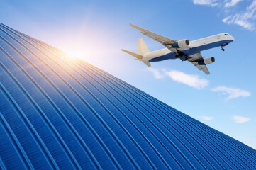 Fototapeta na wymiar Freight airplane flying above above the roof of the hangar warehouse in the rays of the bright sun. Logistics supply chain management and international goods export concept.
