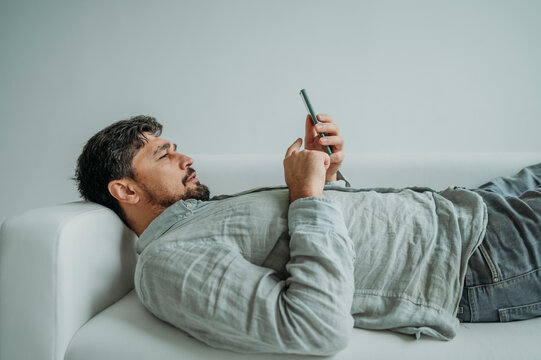 Man Using Smart Phone Lying On Sofa Against White Background