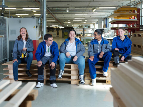Happy apprentices sitting together on pallets at workshop