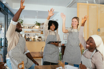 Happy baristas with hands raised celebrating achievement in coffee shop