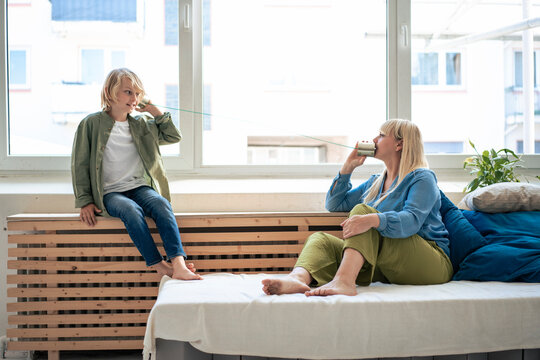Mother talking through tin can phone with son at home