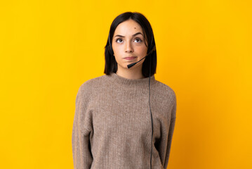 Young telemarketer woman isolated on yellow background and looking up