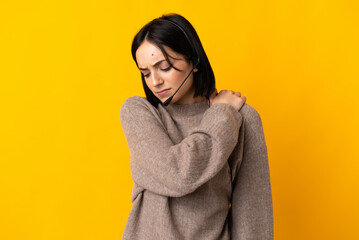 Young telemarketer woman isolated on yellow background suffering from pain in shoulder for having made an effort - obrazy, fototapety, plakaty