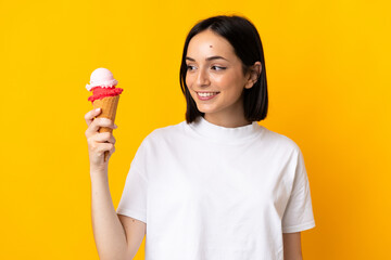 Young caucasian woman with a cornet ice cream isolated on yellow background with happy expression