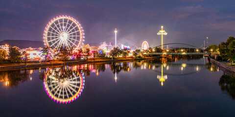 Germany, Baden-Wurttemberg, Stuttgart, Cannstatter Wasen, Panoramic view of glowing Ferris Wheel reflecting in Neckar river at night