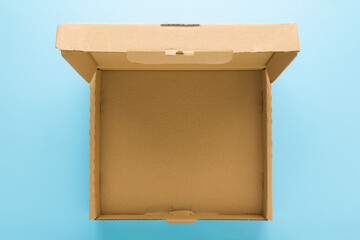 Opened empty brown carton box on light blue table background. Pastel color. Closeup. Empty place...
