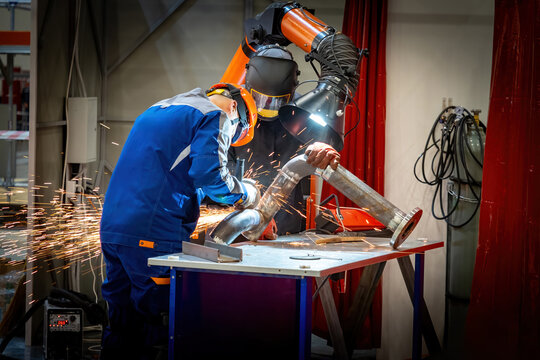 Man workers are repairing fragment pipeline. Craftsmen work in production factory. Guys use grinding machine. Sanding weld seam on pipe. Repair pipeline at factory. Workers near table for welding