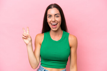 Fototapeta premium Young caucasian woman isolated on pink background smiling and showing victory sign