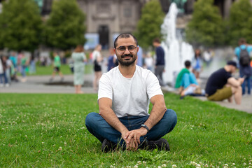 The man sitting and smiling in front of the Berliner dom green grass in sunny weather. Traveling concept. Selectively focused on the man. 