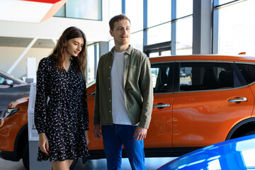 A young couple chooses a new car at a car dealership. Buying a long-awaited car. Joint family purchase.