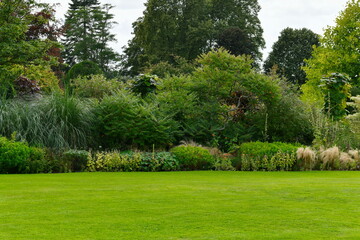 Fototapeta na wymiar Scenic view of a beautiful English style landscape garden with a green mowed grass lawn and a colourful flower bed