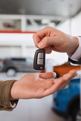 Close-up of the hands of the seller who is handing over the car key to the buyer against the background of cars in the showroom.