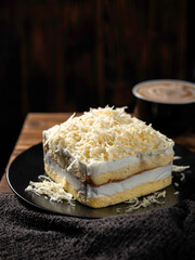 Layered cheese cake with grated cheese sprinkles is neatly presented on a plate, isolated against a wooden table background motif.