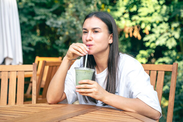 Woman drinking matcha latte while sitting at cafe outdoors.