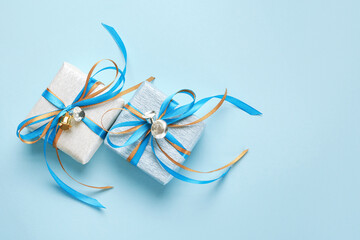 Two gift boxes wrapped in white and blue silver paper with blue and gold ribbon bows and bells. Blue background, top view. Christmas and New Year gifts, Boxing Day.