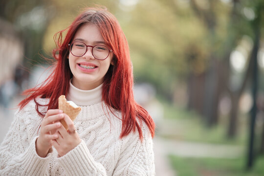 Happy girl in a white sweater holds ice cream in a waffle cone in her hands.