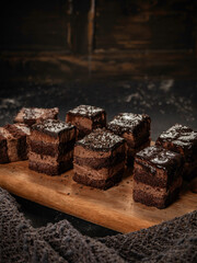 A chocolate sponge cake drizzled with chocolate sauce is served on a wooden cutting board, isolated against a kitchen background.