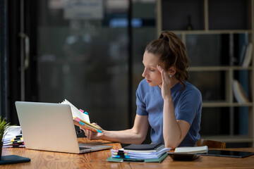 Business woman sitting in front of laptop considering work. Stressed out from working hard and writing project plans.