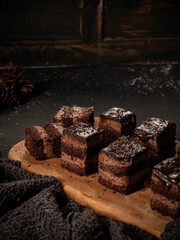A chocolate sponge cake drizzled with chocolate sauce is served on a wooden cutting board, isolated against a kitchen background.