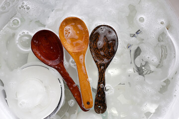 Wooden spoon and dishes in water and bubbles of dishwashing liquid - obrazy, fototapety, plakaty