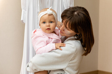 Beauty and fashion concept. Mother and baby daughter in white shirts in a home bathroom, doing spa...