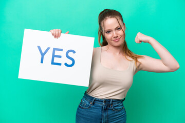 Young caucasian woman isolated on green background holding a placard with text YES doing strong gesture