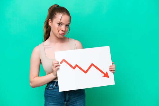 Young caucasian woman isolated on green background holding a sign with a decreasing statistics arrow symbol with sad expression