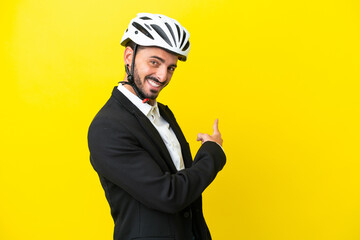 Business caucasian man with a bike helmet isolated on yellow background pointing back