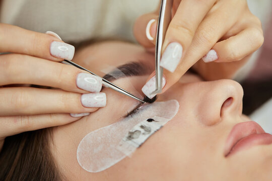 Beautiful female face during lash extension procedure in salon. Fake eyelashes