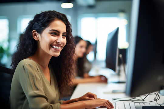 Portrait of Enthusiastic Hispanic Young Woman Working on Computer in a Modern Bright Office, Confident Human Resources Agent Smiling Happily While Collaborating Online with Colleagues