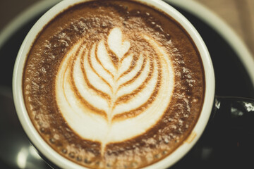 Closeup white cup of hot coffee latte on wood background in restaurant.Leaf tree texture coffee latte art make by barista on best of menu in the coffee shop.Soft focus