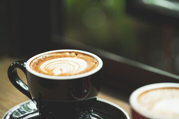 Closeup black cup of hot coffee latte on wood background in restaurant.Leaf tree texture coffee latte art make by barista on best of menu in the coffee shop.Soft focus