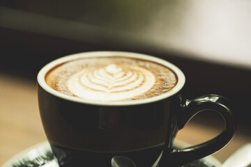 Closeup black cup of hot coffee latte on wood background in restaurant.Leaf tree texture coffee latte art make by barista on best of menu in the coffee shop.Soft focus