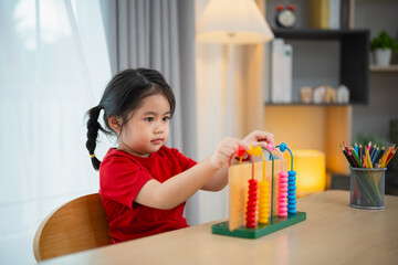 Young cute Asian baby girl wearing red t-shirt is learning the abacus with colored beads to learn...