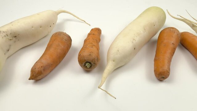 Fresh raw daikon radishes and carrots lie in a row on a white table