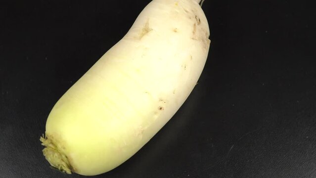 Fresh raw daikon radish lies on a black table