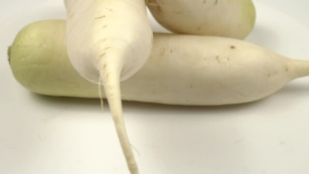 Fresh raw daikon radishes lie on a white table
