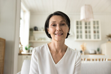 Attractive middle-aged woman smile looks at camera sit on sofa, having videoconference remote talk to family or grown-up children living abroad, enjoy communication using modern tech, profile picture - Powered by Adobe