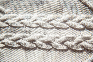 Fototapeta na wymiar White knitted fabric texture with a pattern of braids. Close-up abstract background