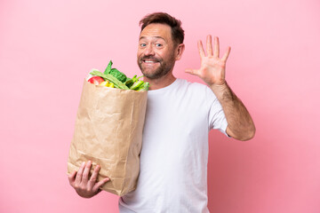 Middle age man holding a grocery shopping bag isolated on pink background counting five with fingers