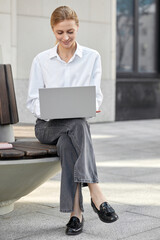 Portrait of a stylish young business lady dressed in a white blouse and checking email on a laptop
