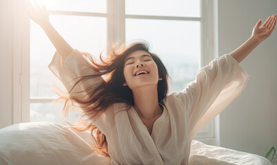 Fototapeta premium Joyful Asian woman awakens, stretching in a sunlit bedroom.