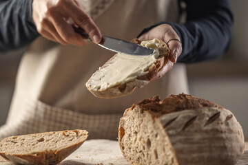A woman makes delicious bread, spreads cream cheese with a cutlery knife - Close up. Woman hands spreading cream cheese on bread slice. - obrazy, fototapety, plakaty