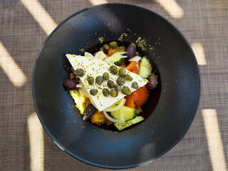 Plate of Greek salad placed on a table illuminated by rays of light with a straw tablecloth.