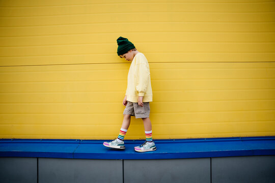 Boy wearing sweatshirt looking down and walking by yellow wall