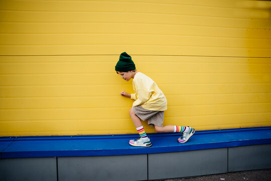 Playful boy wearing sweatshirt crouching in front of yellow wall
